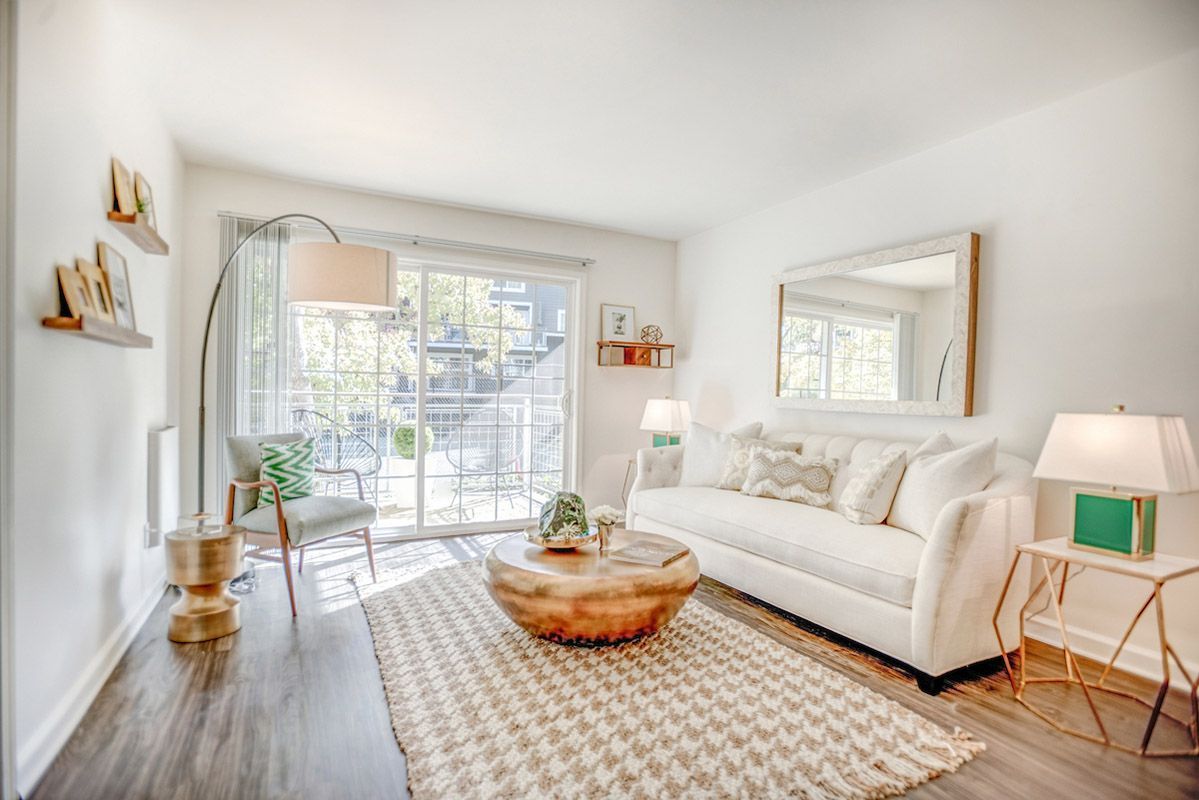 Bright living room with a white sofa, sliding glass door to a balcony, and a geometric rug.