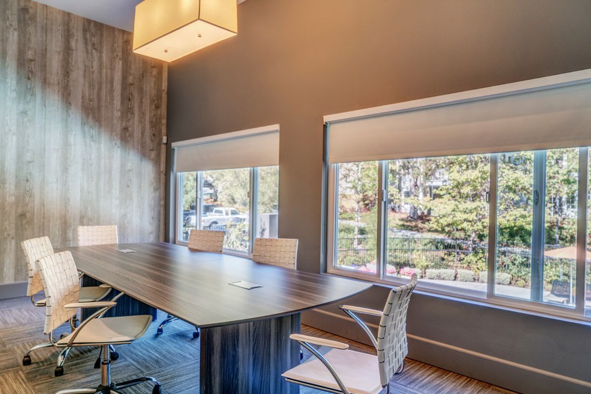 Conference room with a large wood table, white chairs, and big windows.