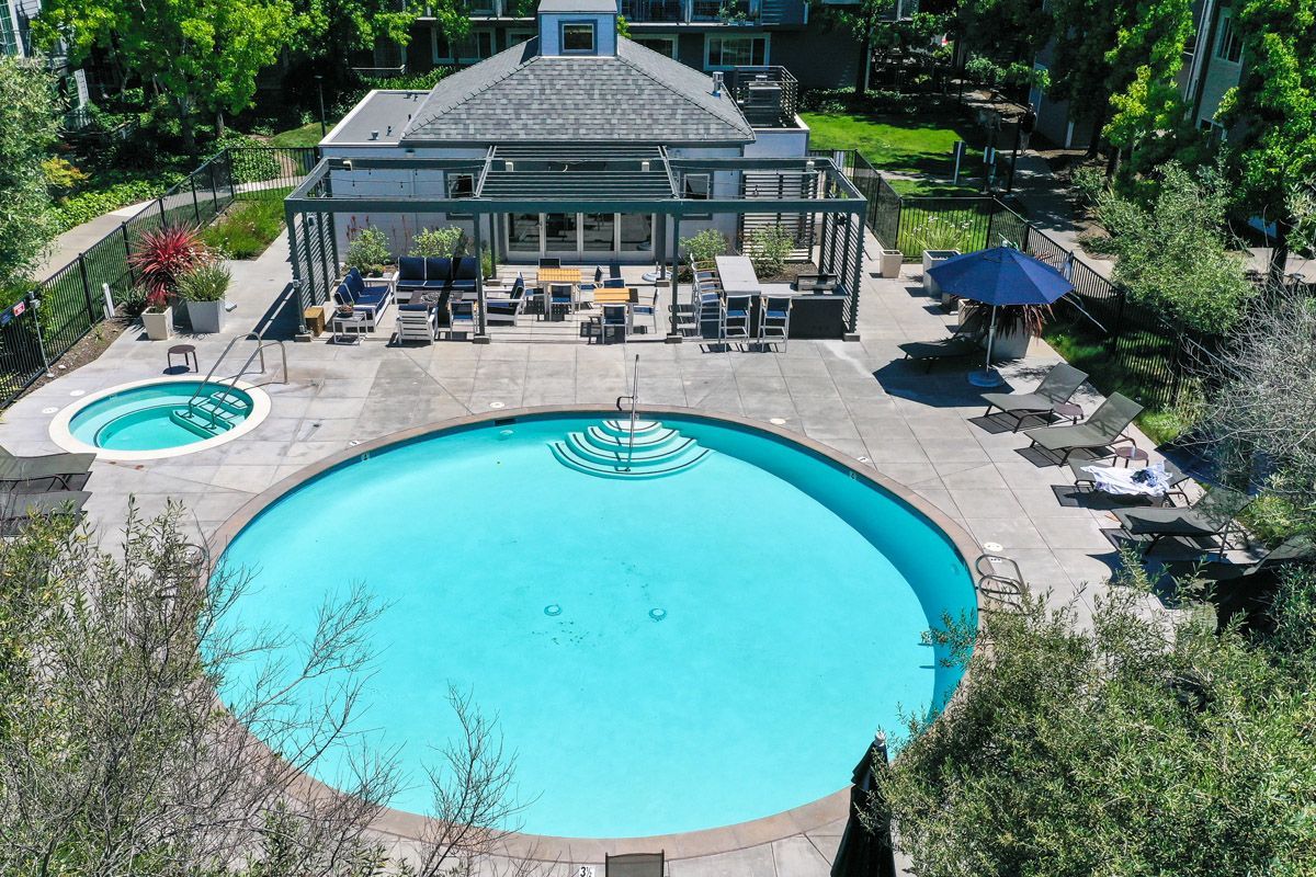 Aerial view of a large outdoor community pool with a circular spa, lounge chairs, and a shaded seating area.