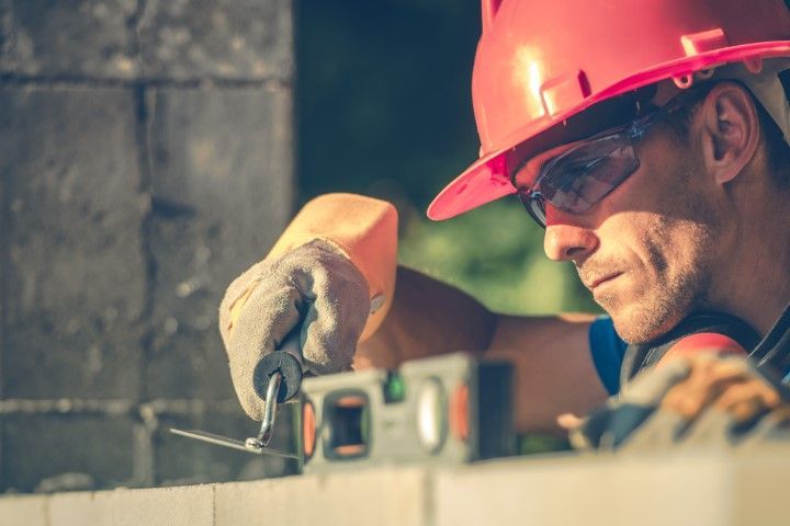 Worker in red hard hat and safety glasses measuring material with a tool at a worksite