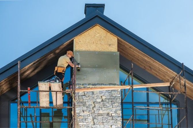 Worker repairing the peak of a house roof on scaffolding under a blue sky