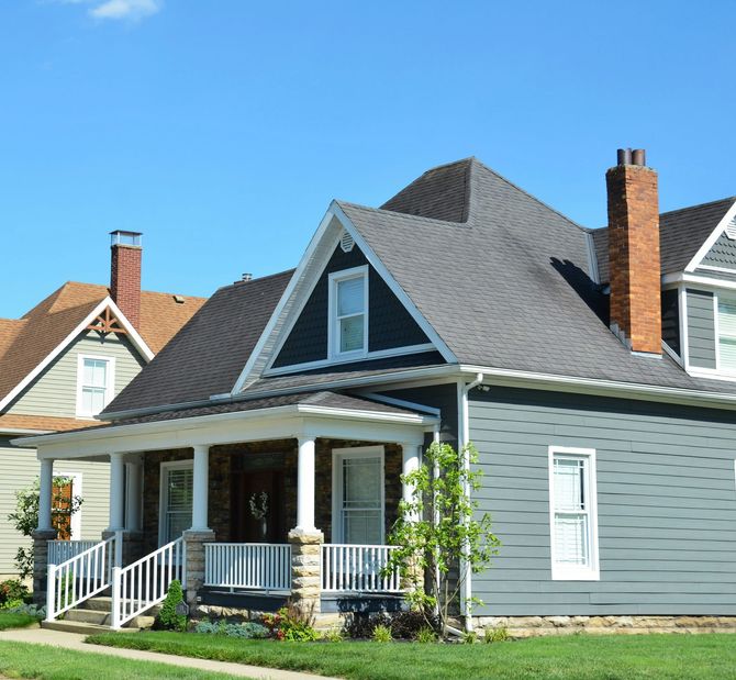 Gray house with a front porch, white trim, and a steep shingled roof on a sunny day