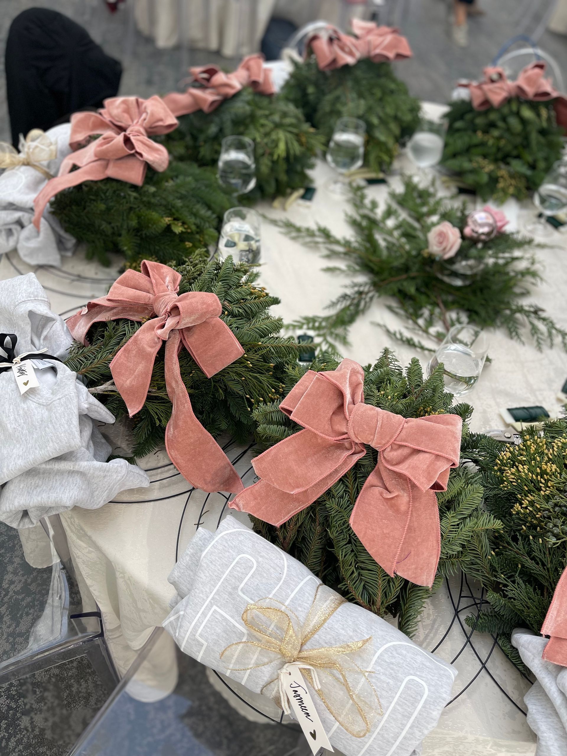 Table setting with evergreen wreaths and pink bows, featuring gifts.
