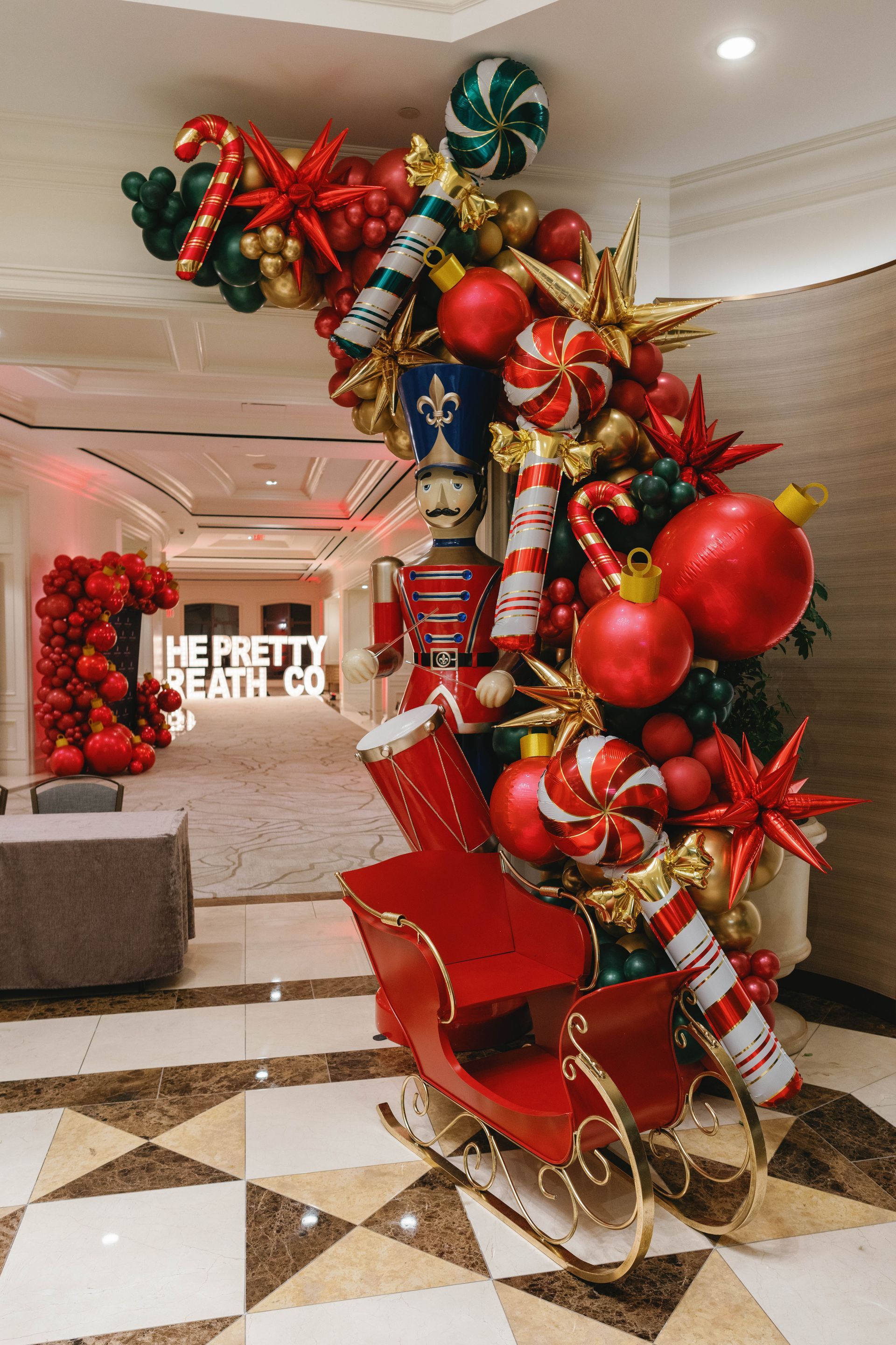 Christmas display: Red sleigh, arch of ornaments, nutcracker, candy canes, green and gold balloons.