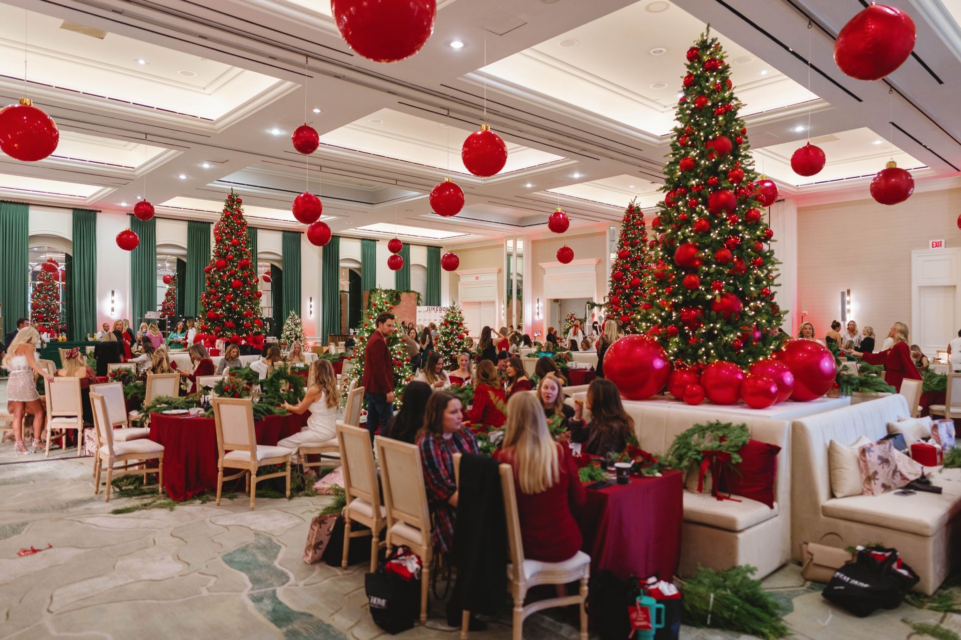 Festive room decorated for Christmas. People seated at tables, trees, and red ornaments.