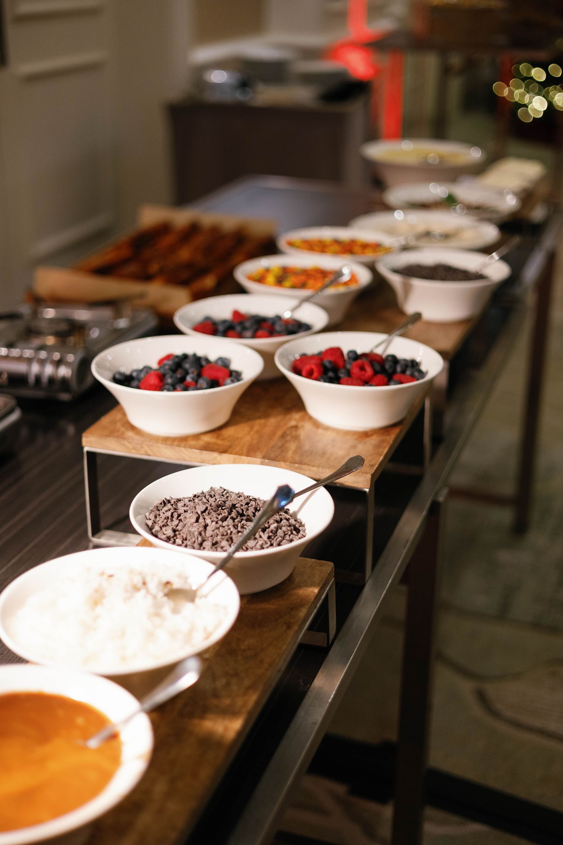Buffet table with bowls of toppings: berries, chocolate chips, coconut, and other breakfast items.