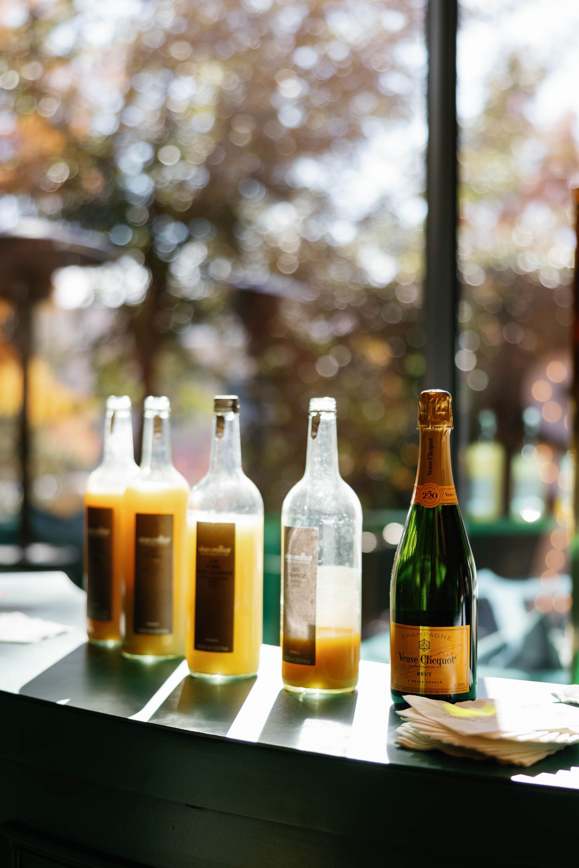Bottles of juice and champagne on a bar, with an out-of-focus outdoor background.