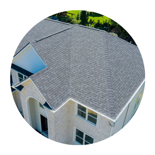 Aerial view of a house with a gray shingle roof and white exterior surrounded by trees