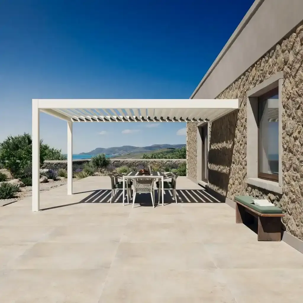 Patio moderno con pergola bioclimatica, tavolo da pranzo e vista sulle montagne, accanto a una casa in pietra.