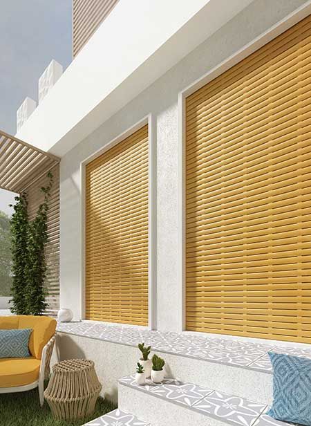 Patio moderno con tende di bambù gialle, pareti bianche e sedute in vimini sotto la luce del sole.