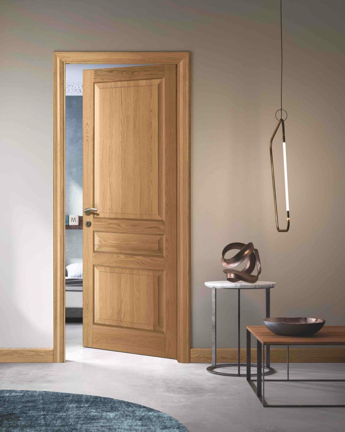 Porta di legno aperta in una stanza minimalista sui toni del beige con una cinghia appendiabiti, un tavolino e una panca.