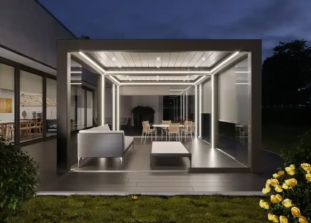 Pergola bioclimatica con eleganti sedute bianche e luci soffuse al crepuscolo, visto da un prato.