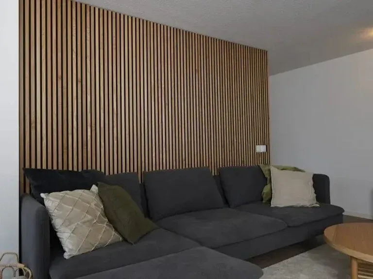 Divano grigio in un soggiorno moderno con parete decorativa in legno a righe pannello fonoassorbente e tavolino rotondo.