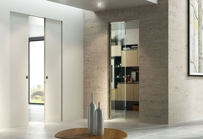 Ingresso moderno e minimalista con porte scorrevoli bianche, mobiletto con specchio e vasi decorativi su un tavolo rotondo.