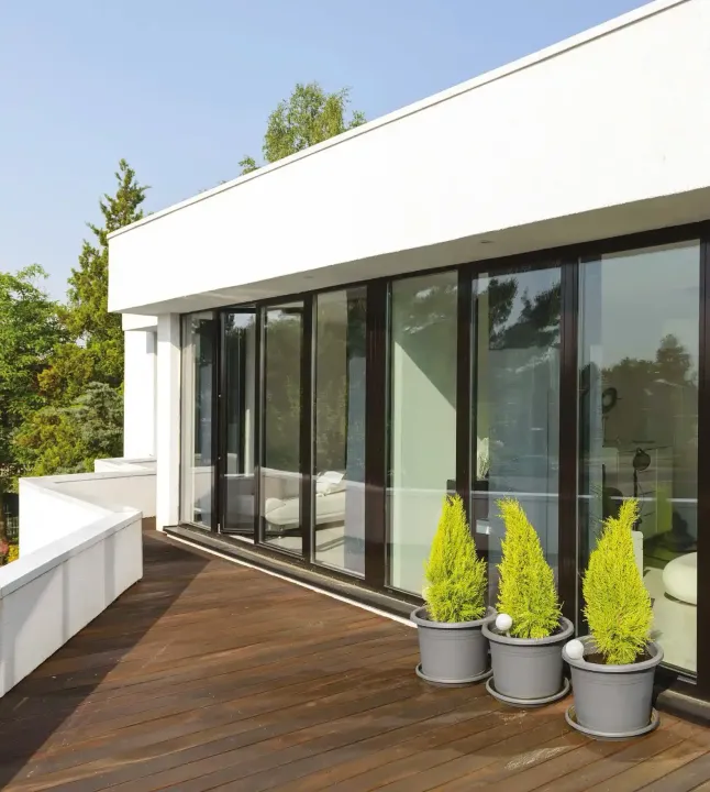 Terrazza moderna con porte scorrevoli in vetro, pavimento in legno e piante in vaso sul balcone.