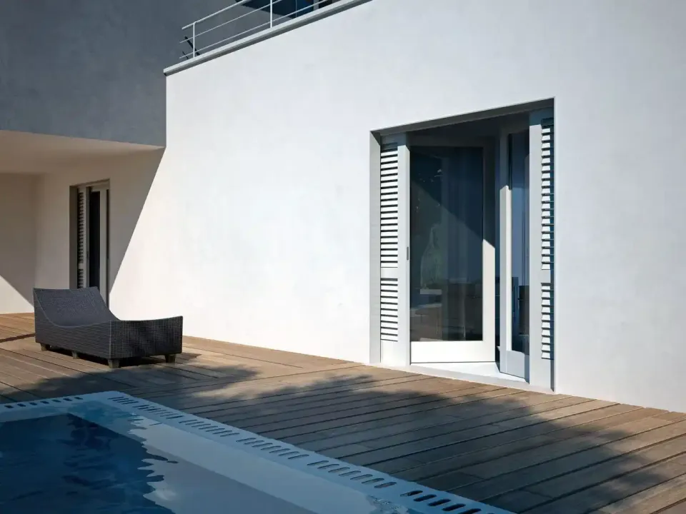 Patio di una moderna villa bianca con piscina, sdraio e porte finestre che si affacciano sull'acqua.
