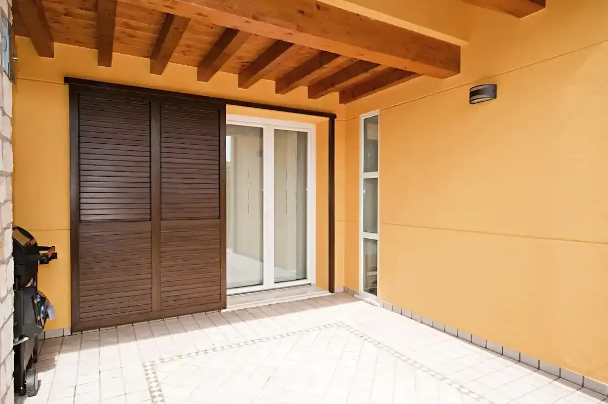 Patio coperto con pareti gialle, travi a vista in legno e porte scorrevoli in vetro.