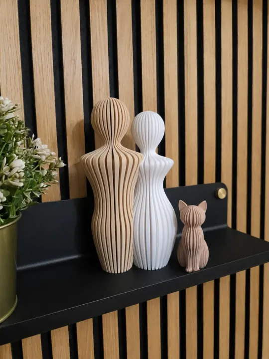 Stampa 3D, tre statuette di ceramica a righe su una mensola nera, appoggiate a una parete a doghe di legno.