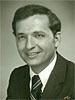 Man in dark suit, smiling, wearing tie. Studio portrait.