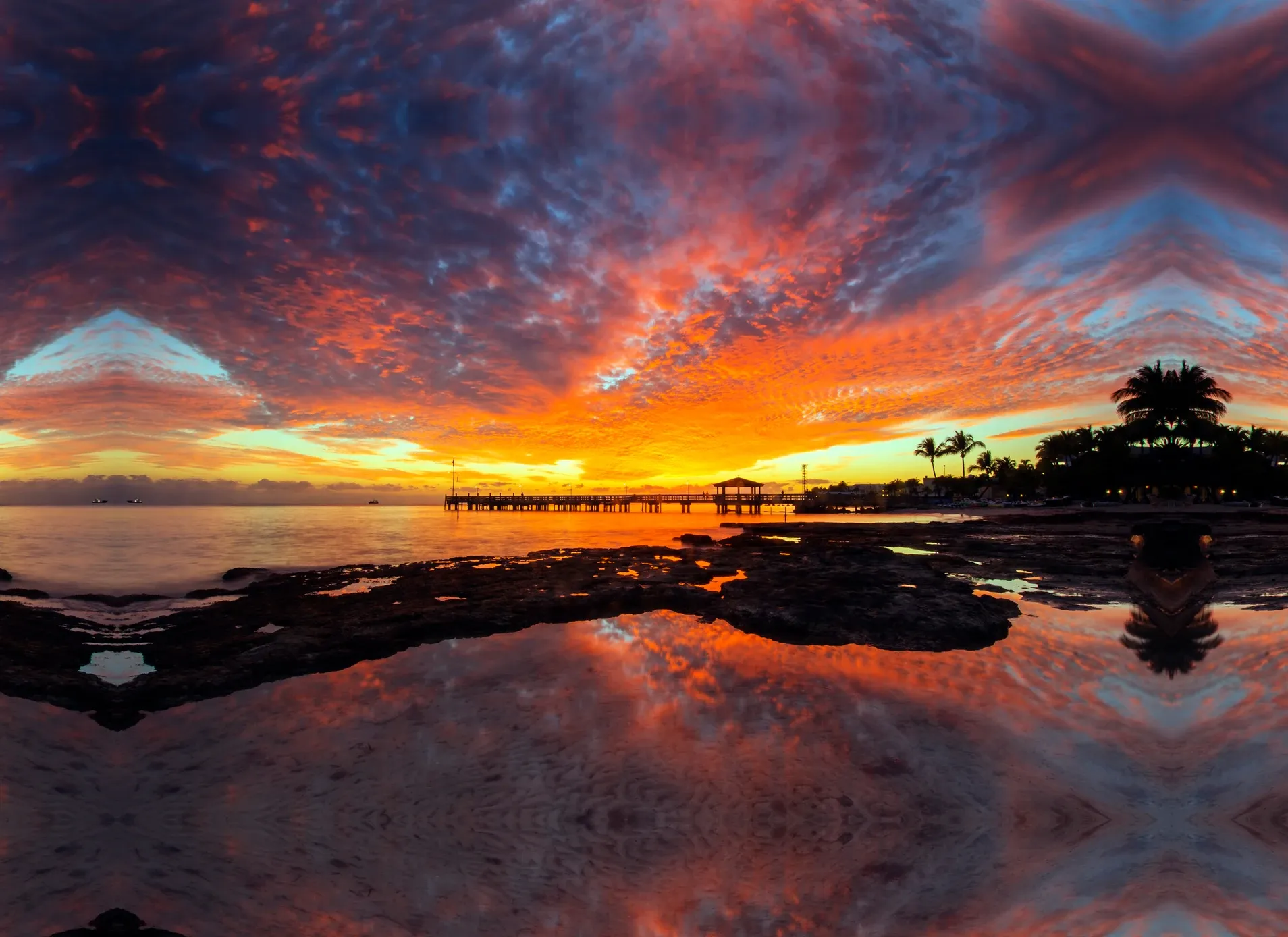 Vibrant sunset over calm shoreline with palm trees and reflections in the water