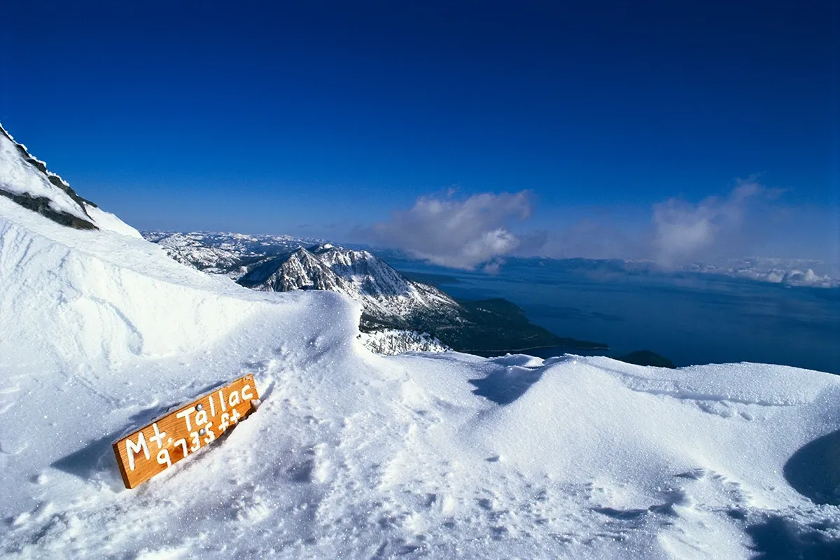 Snowy mountain overlook with distant peaks and a blue sea under a clear sky