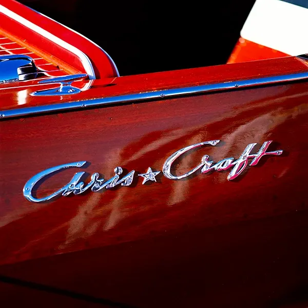 Close-up of a red Chris-Craft boat hull with chrome logo and blue trim