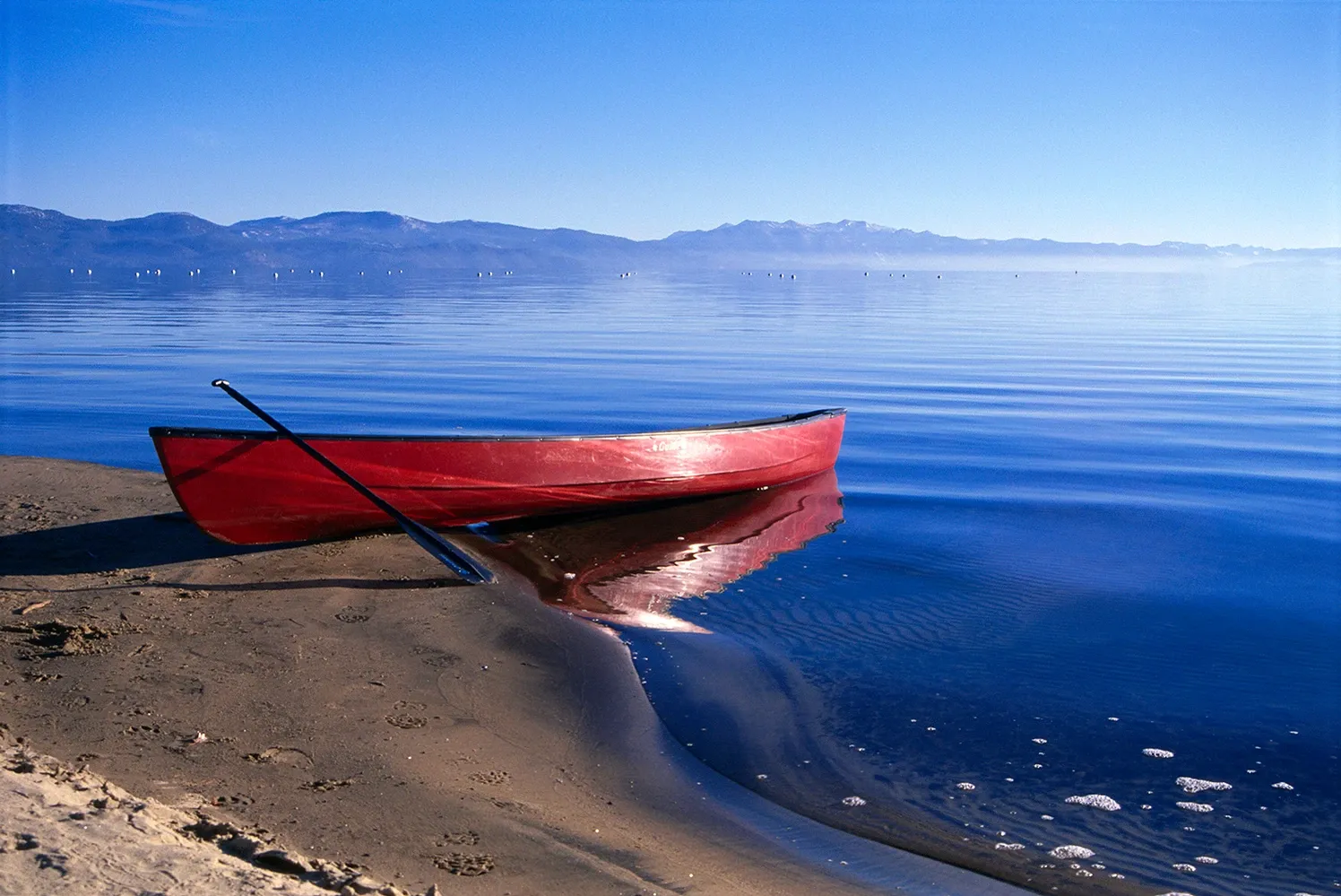 Red rowboat on a sandy beach beside calm blue water under a clear sky