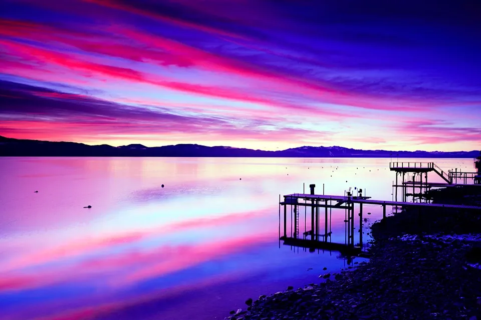 Vibrant purple-pink sunset over a calm lake with a dock and silhouetted shoreline