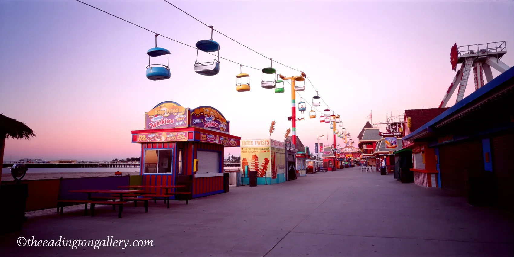 Empty amusement park walkway with colorful cable cars overhead at sunset