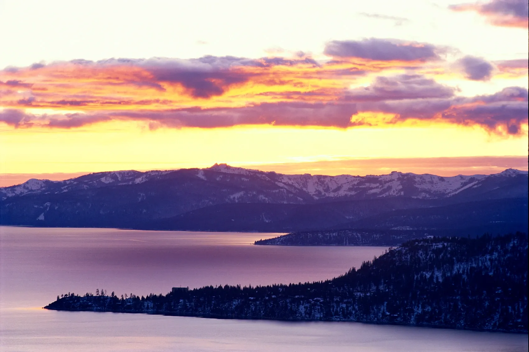 Sunset over a calm bay with snow-covered hills and purple clouds