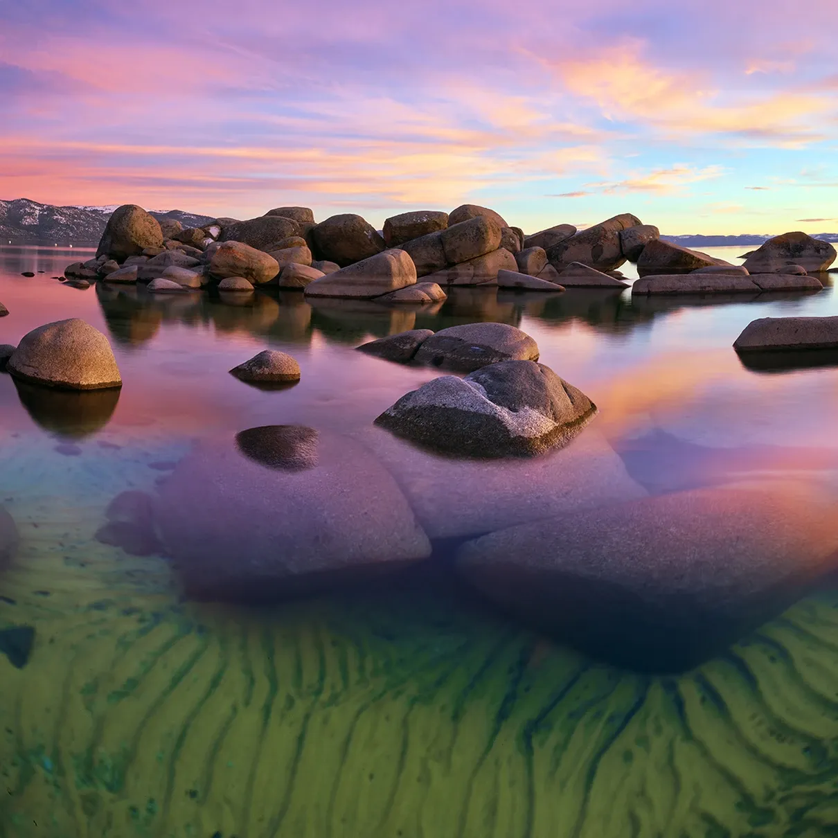 Rocks in calm tide pools at sunset, with pink sky reflections and green sand below water