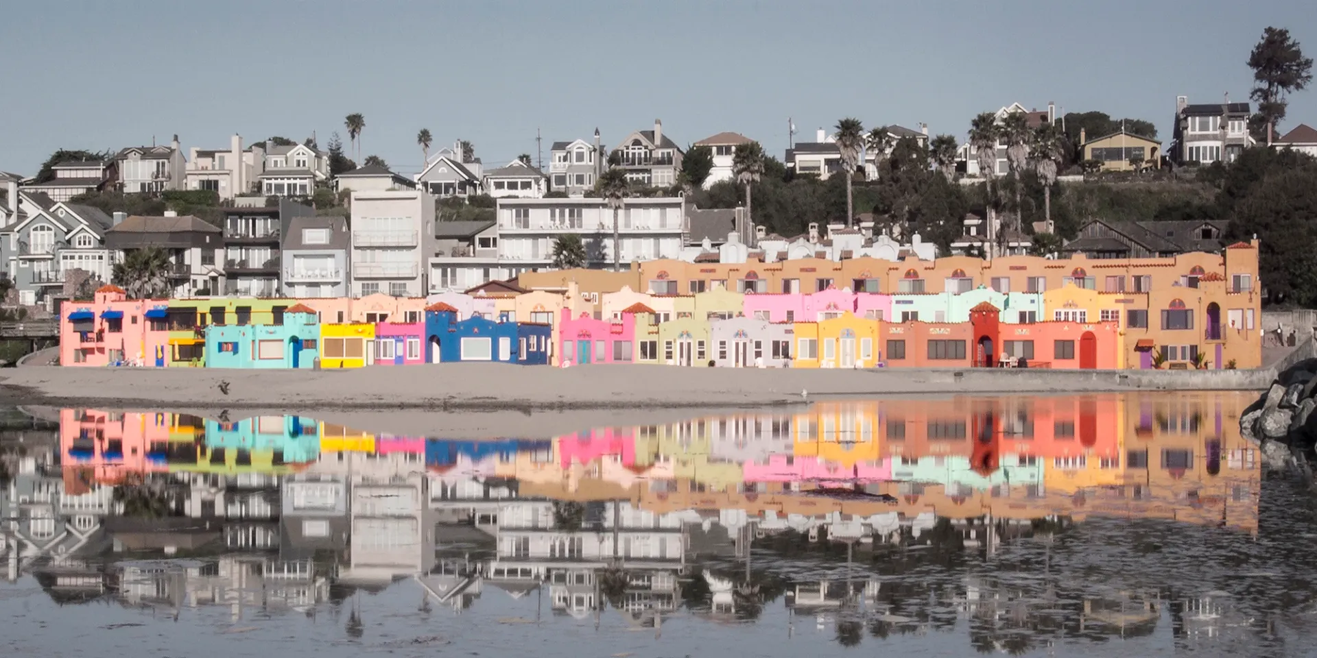 Colorful seaside row of buildings with reflections in calm water under a clear sky
