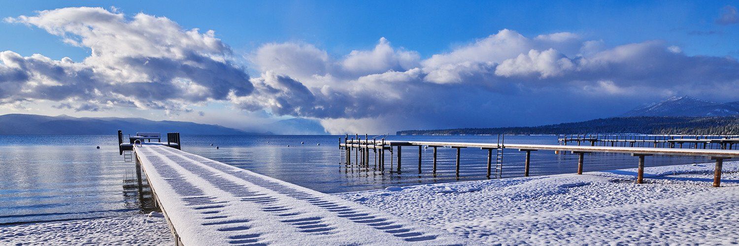 Snowy pier extending into a calm blue lake under a cloudy winter sky