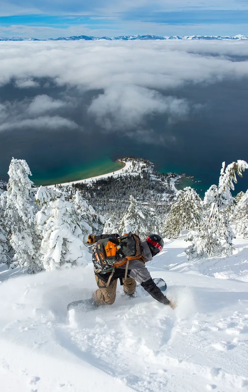 Snowboarder carving powder on a snowy mountain above a cloud-covered coastline