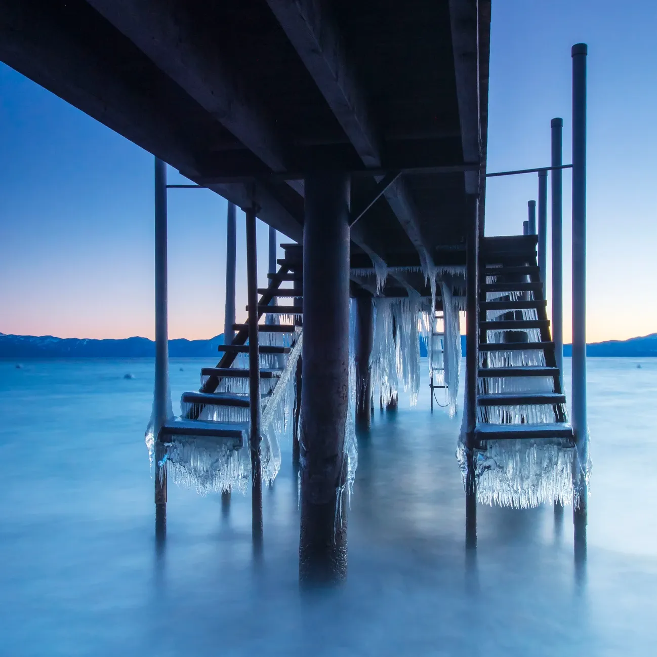 Low pier over calm blue water at dusk, with staircases descending into the sea