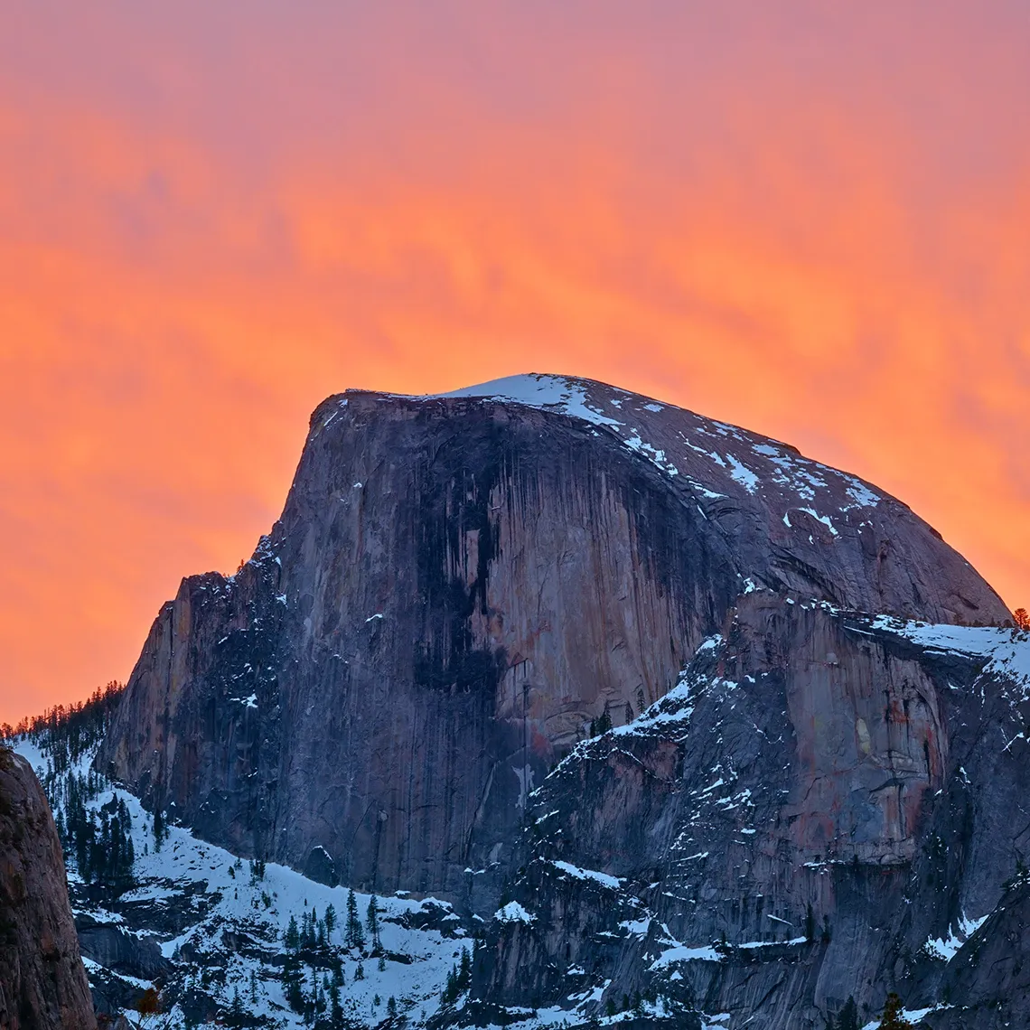 Snow-covered Half Dome at sunset under a vivid orange sky