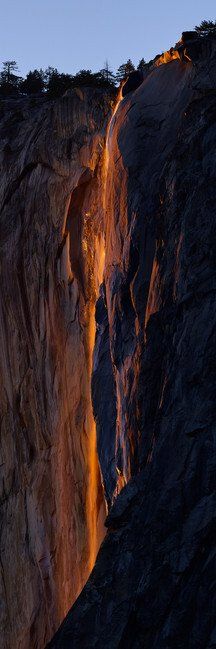 Sunlit orange waterfall cascading down a dark cliff at dusk