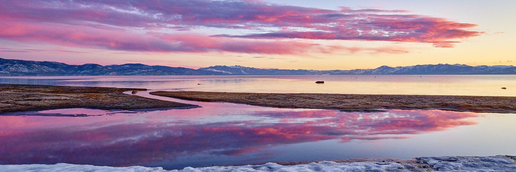 Pink sunset over calm shoreline with colorful clouds reflected in still water