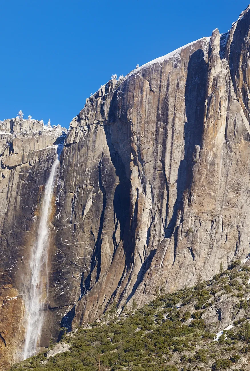 Tall granite cliff with a narrow waterfall under a bright blue sky