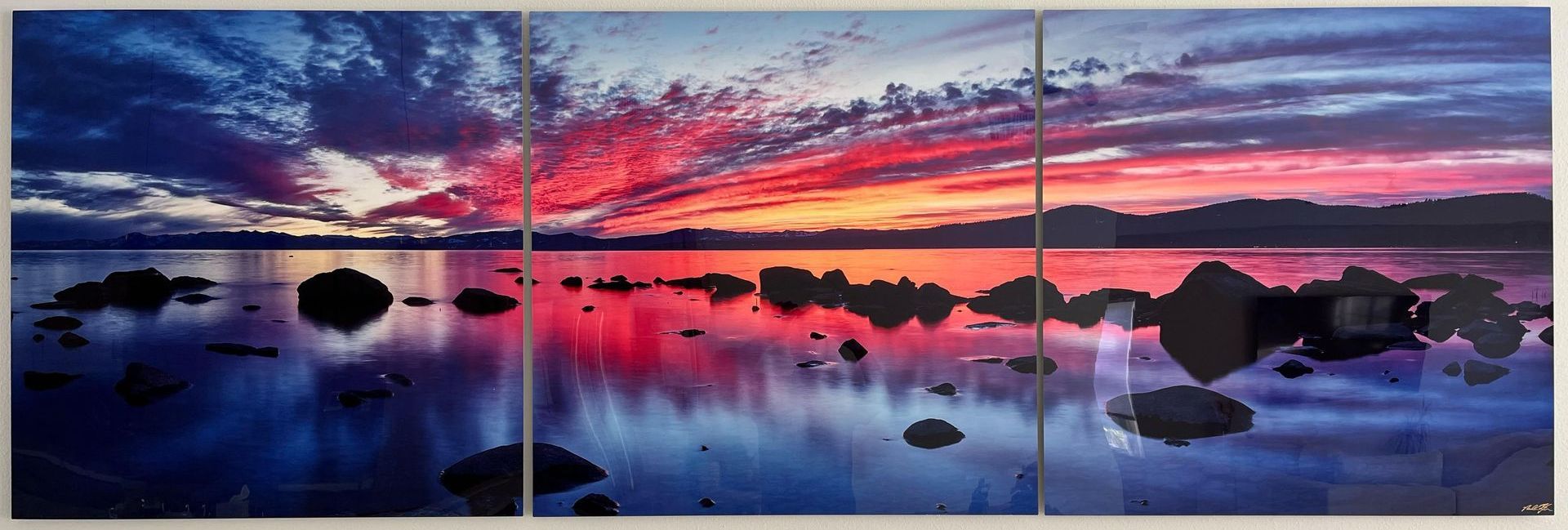 Pink and purple sunset over calm water with rocks and reflections