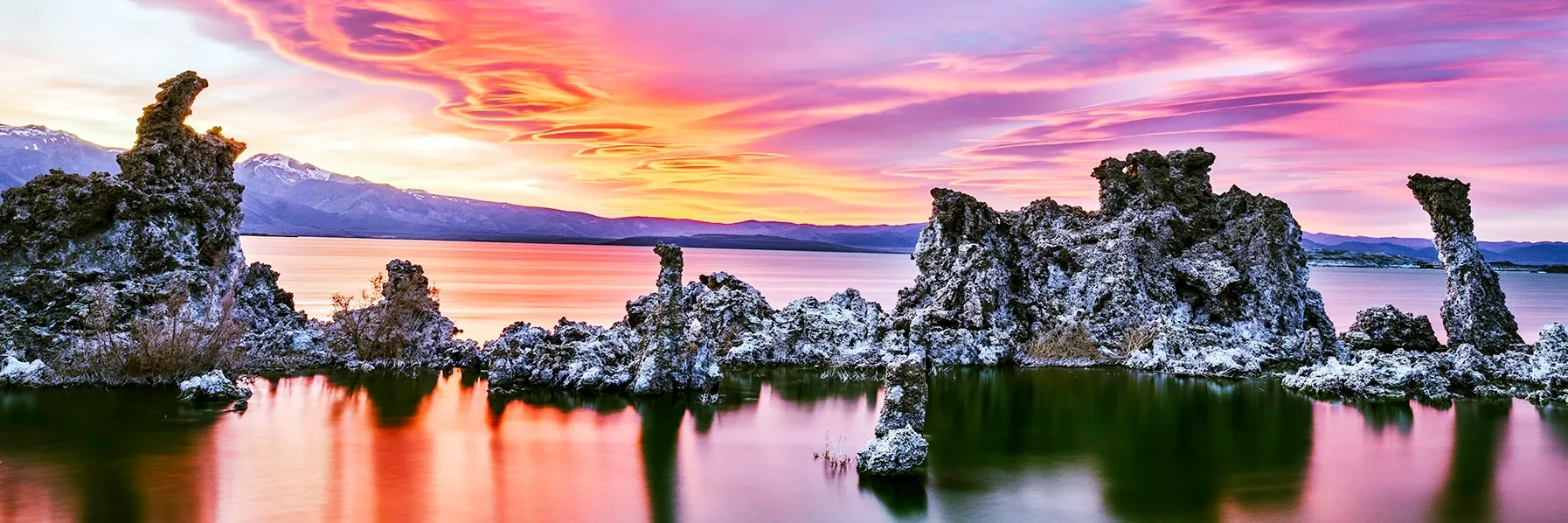 Sunset over a calm lake with pink clouds and silhouetted trees on small islands