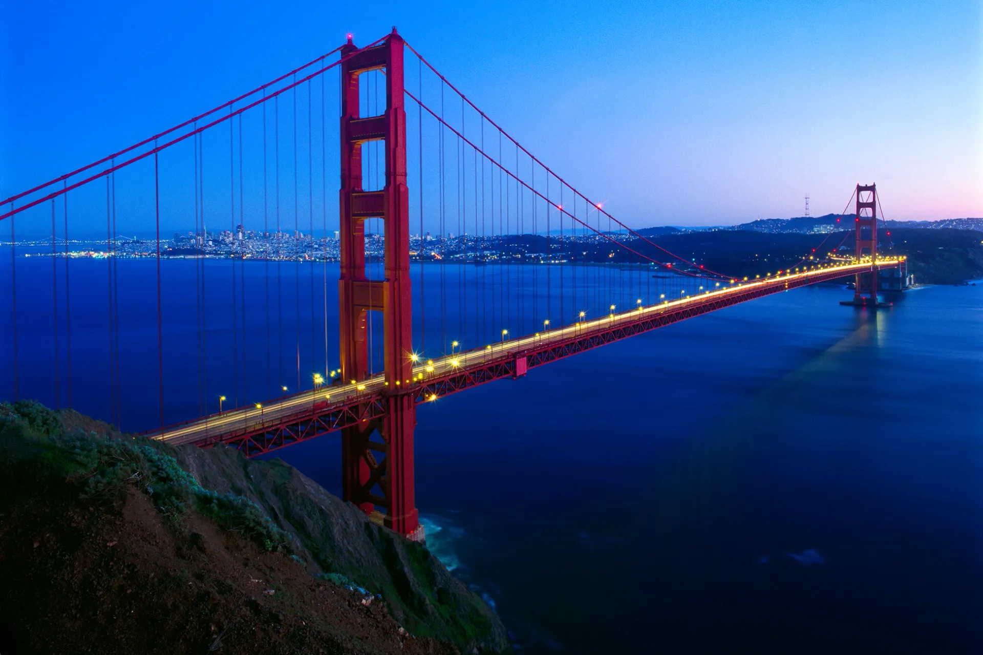 Golden Gate Bridge at dusk, lit in red and spanning blue water under a twilight sky