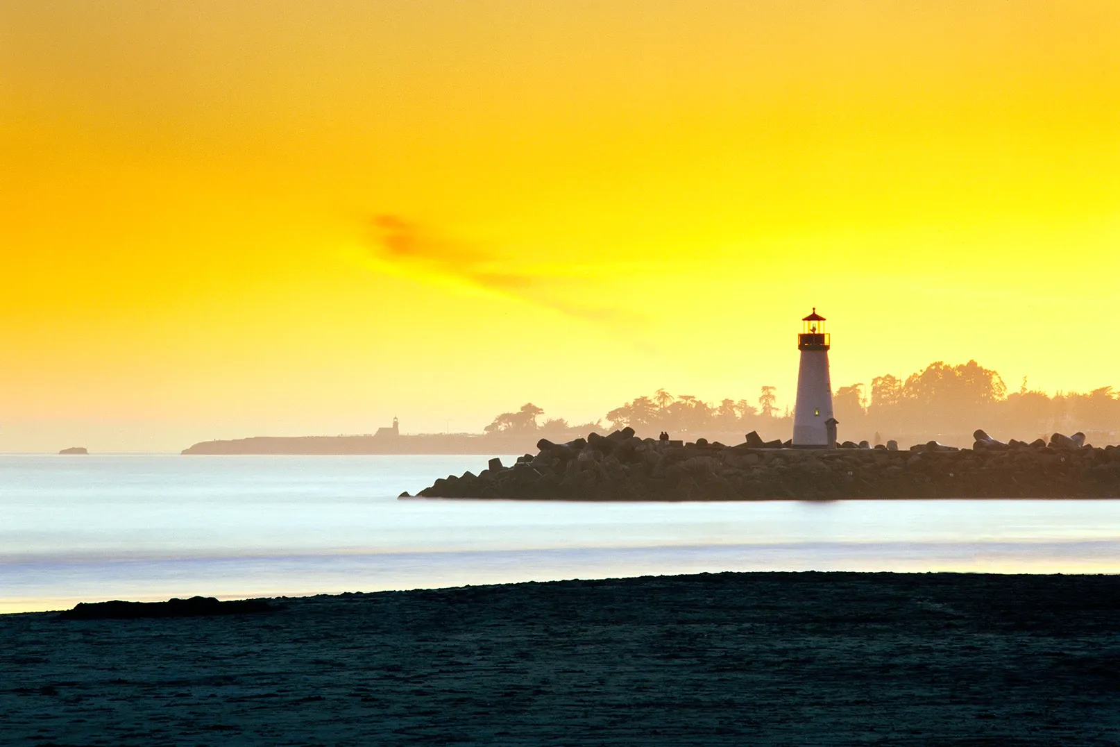 Sunset over calm sea with a lighthouse silhouetted on a distant shoreline