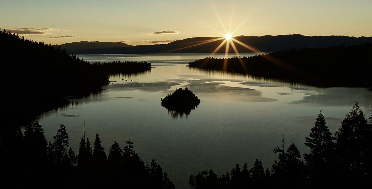 Sunrise over a calm lake with dark silhouetted trees and a small island