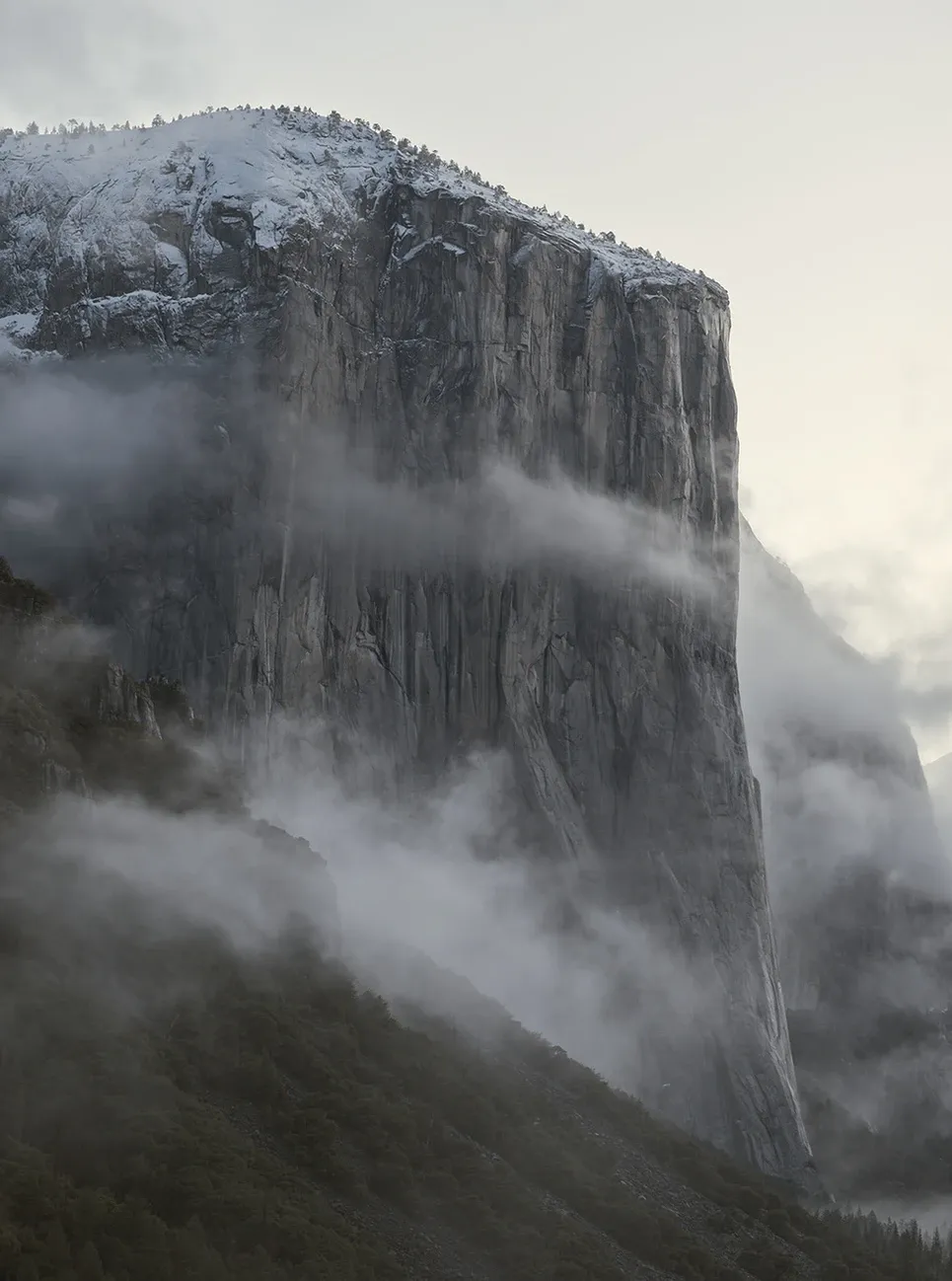 Steep, snow-dusted mountain cliff rising through mist and clouds.
