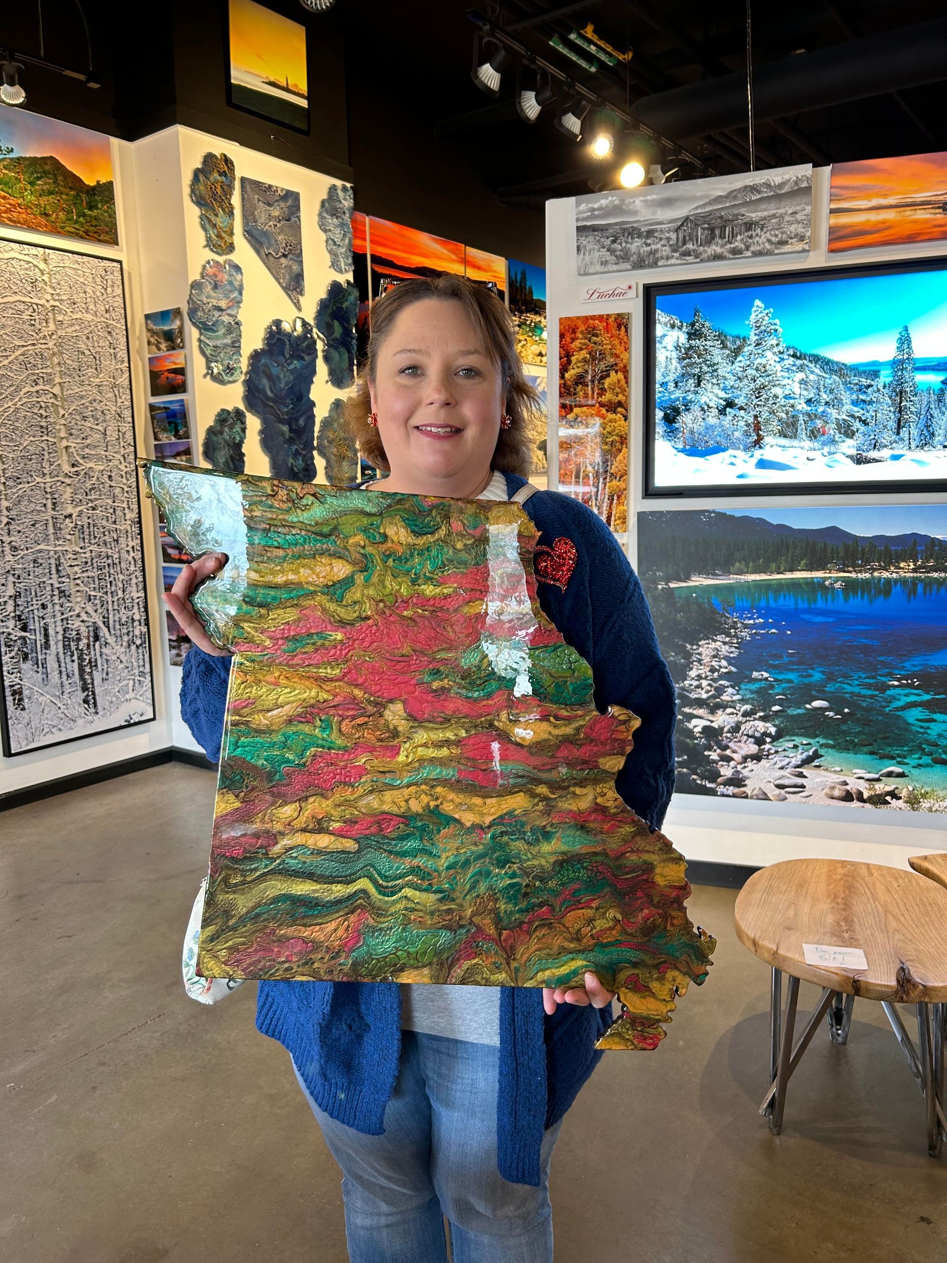 Person holding a colorful quilt-like textile in an art gallery, with landscape paintings in the background