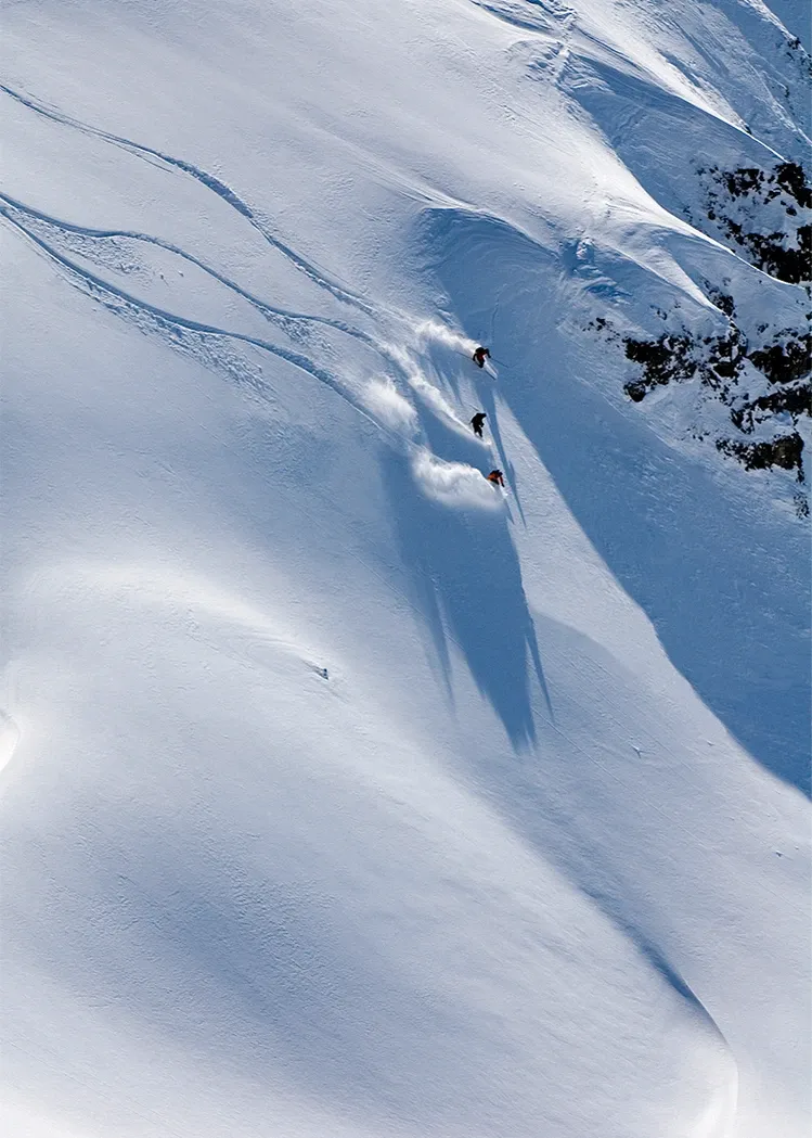 Snow-covered mountain slope with a sharp ridge casting a long shadow.