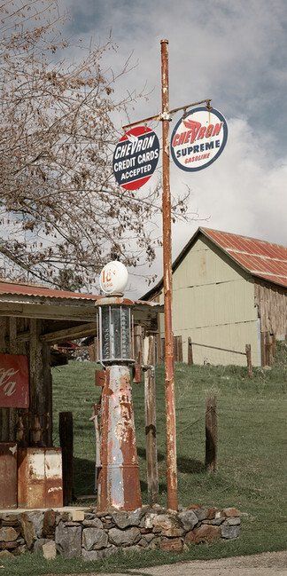 Rusty roadside post with two round signs beside a small house and bare tree in a rural yard