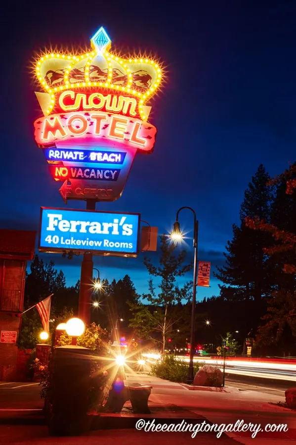 Neon Clown Hotel sign at dusk beside Ferrari’s restaurant sign on a roadside with light trails