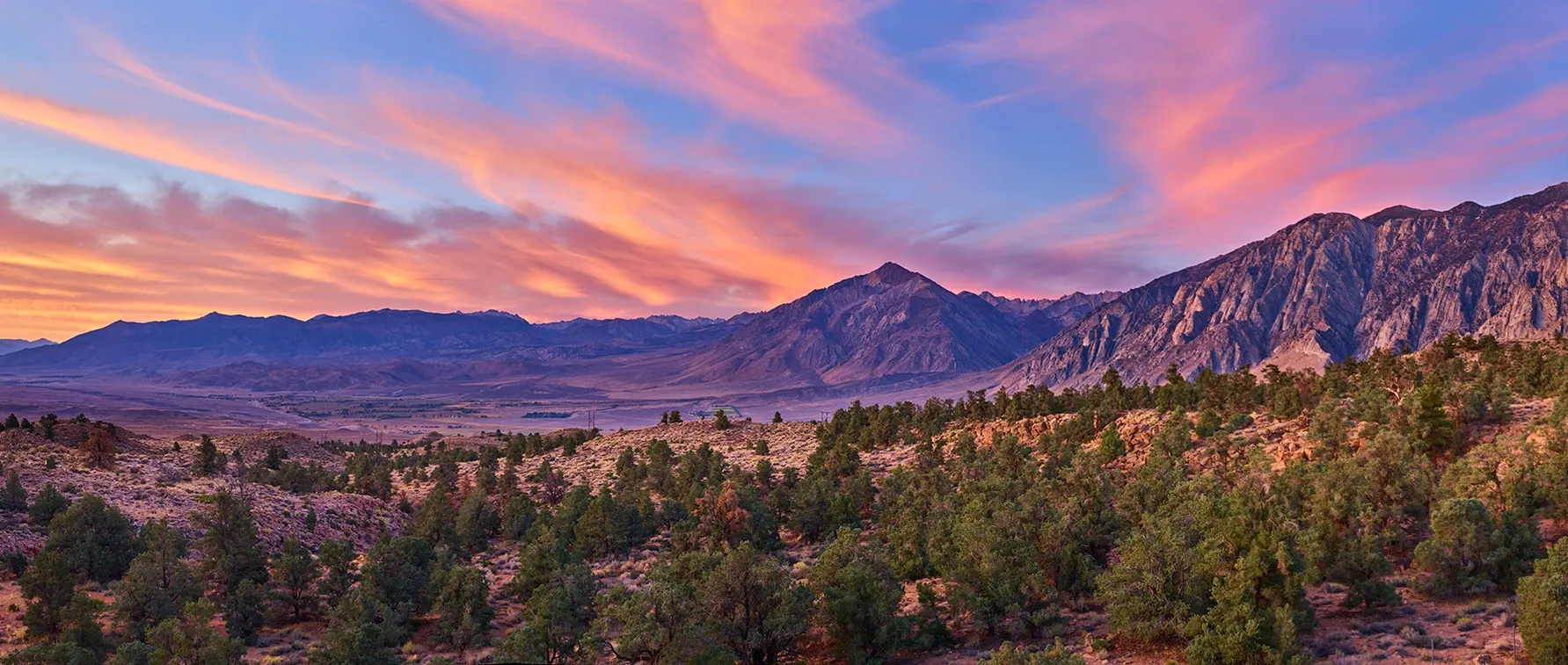 Colorful sunset over rugged mountains and a green valley with pink clouds